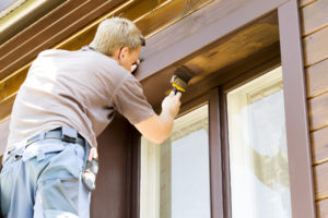 man with paintbrush painting wooden house exterior